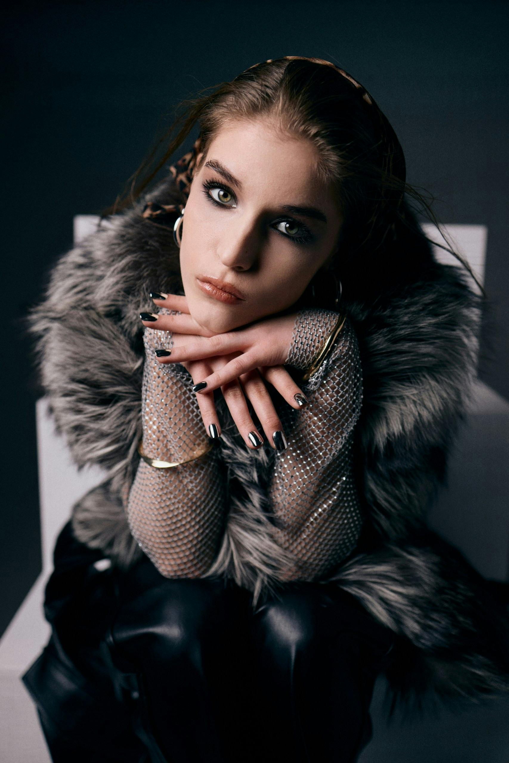 Fashion forward woman in fur coat and mesh gloves sitting indoors.